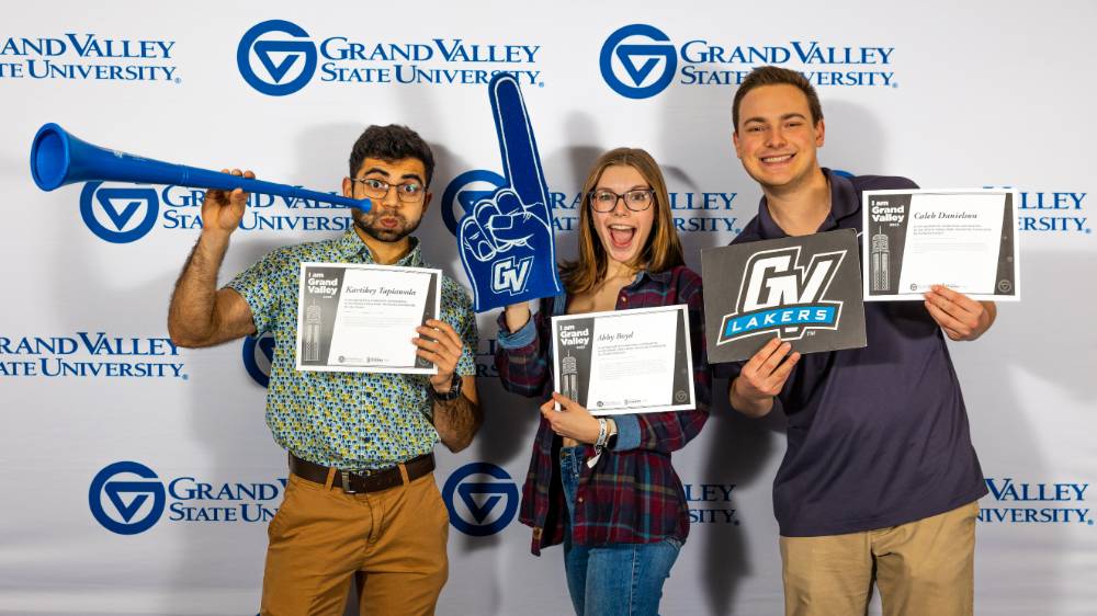 individuals smiling with horn, gvsu lakers sign, and foam finger